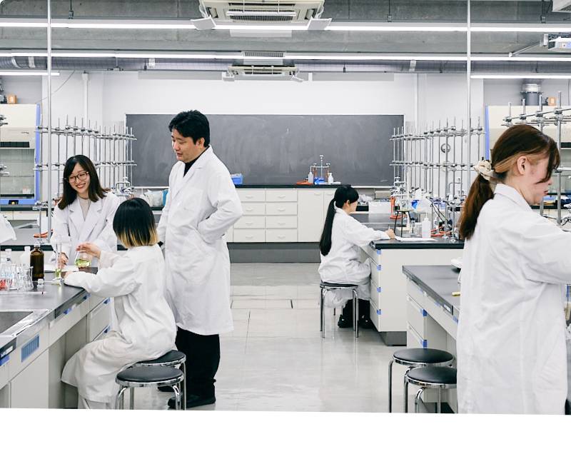 大学の実験室で教授のサポートを受けながら実験を行う白衣姿の学生たち